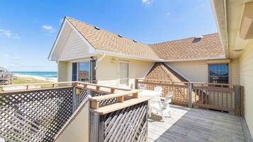 A beach house with a deck, a covered patio, and a view of the ocean.