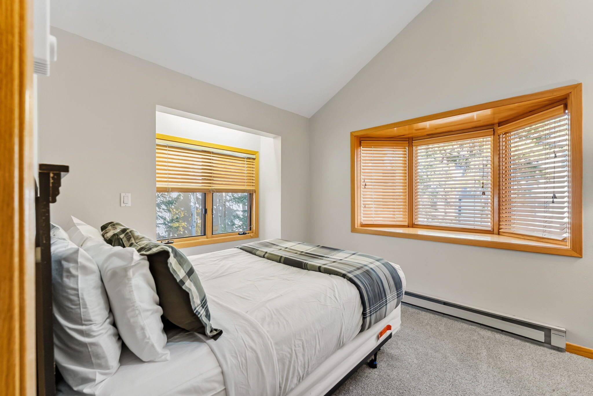 A bedroom with a bed, two windows with blinds, a radiator, and a door.