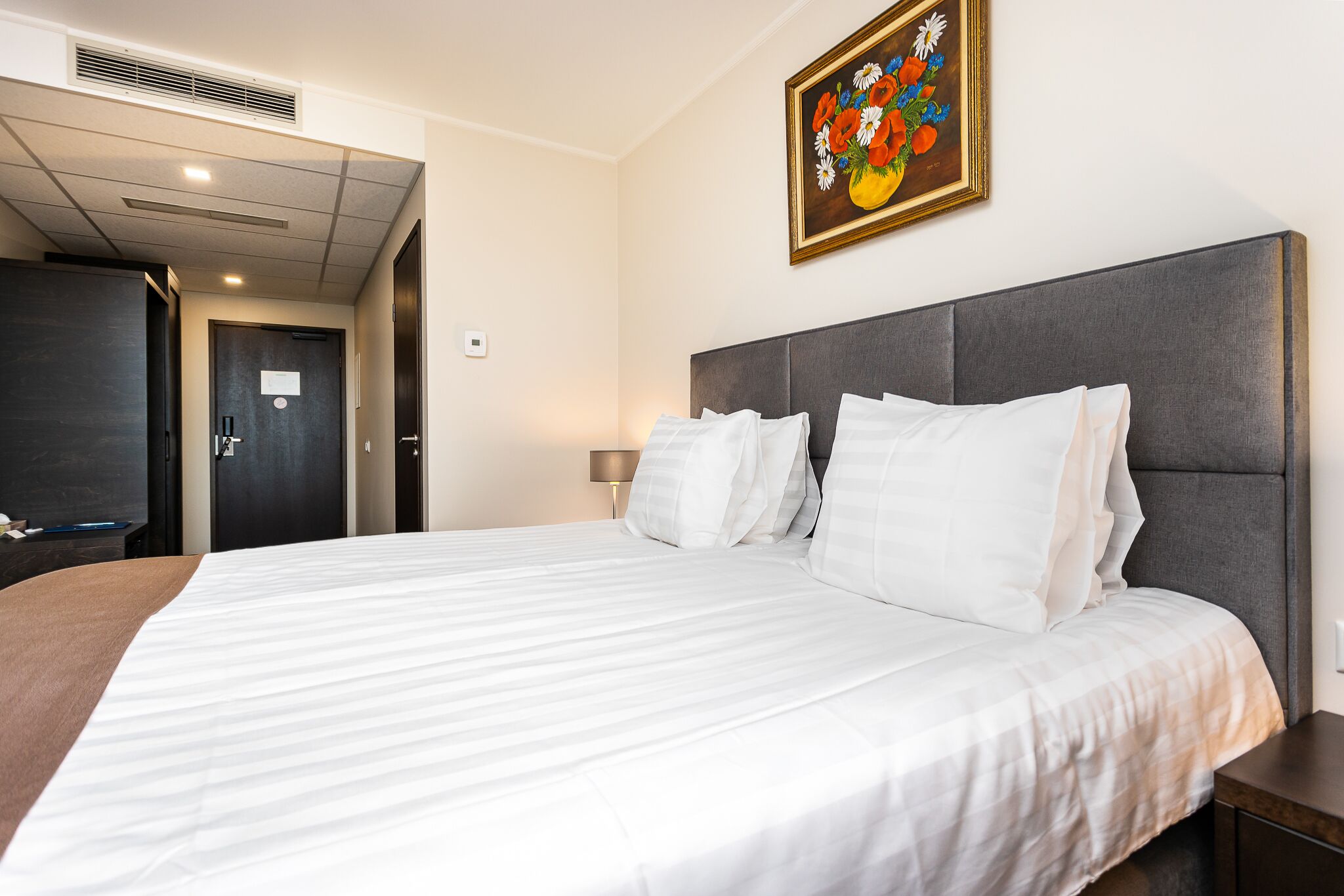 Une chambre d’hôtel avec un grand lit, une tête de lit, une table de chevet, une lampe et un tableau au mur.