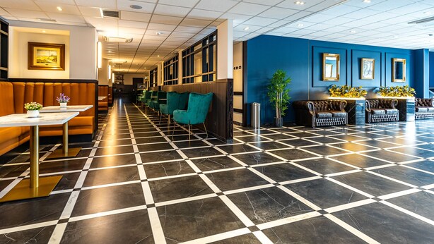 Un hall d’hôtel avec un sol à carreaux, des espaces aménagés pour s’asseoir et des œuvres d’art encadrées accrochées aux murs.