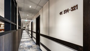 Un couloir d’hôtel avec un sol recouvert de moquette, un comptoir de réception et un mur sur lequel figure un numéro de téléphone.