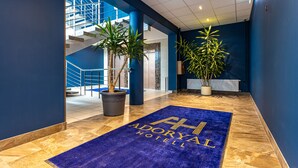 Un hall d’hôtel avec un tapis bleu, un escalier et des plantes en pot.