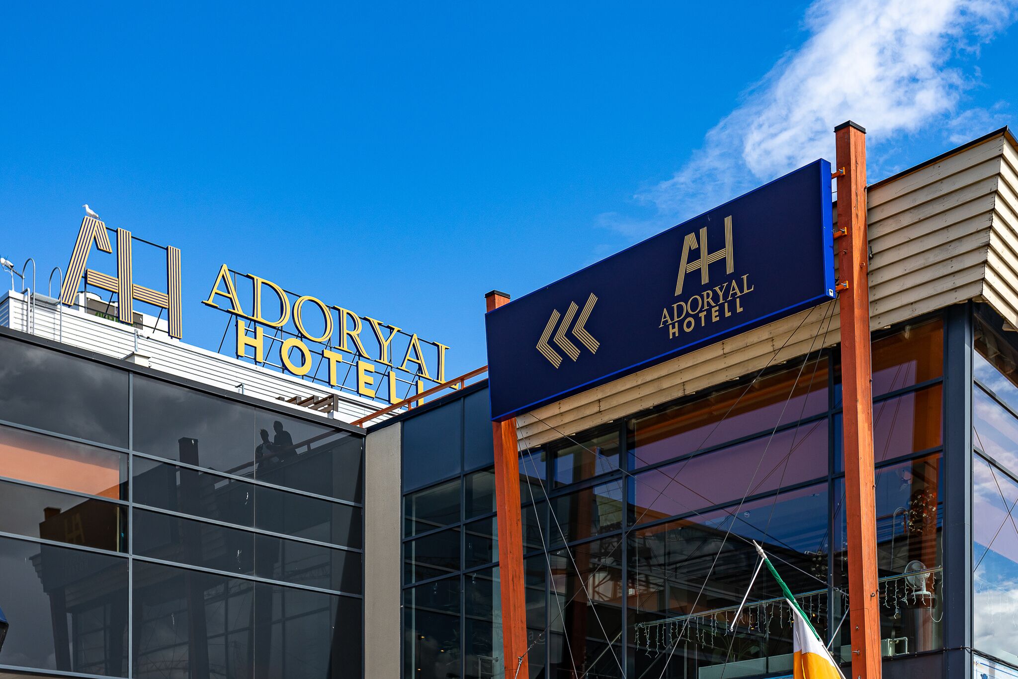 Das Schild des Adoryal Hotels mit modernem architektonischen Design, ausgestattet mit großen Glasfenstern und blauem Himmel im Hintergrund.