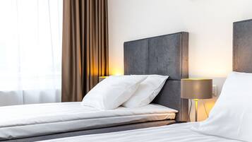 Habitación de hotel con cama, mesita de noche, lámpara y ventana con cortinas.