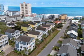 A coastal residential area with multi-story buildings, a clear view of the ocean, and a street lined with houses. - Crabby Paddy: Short Walk To Beach, Sunset Views (Garden City Beach)