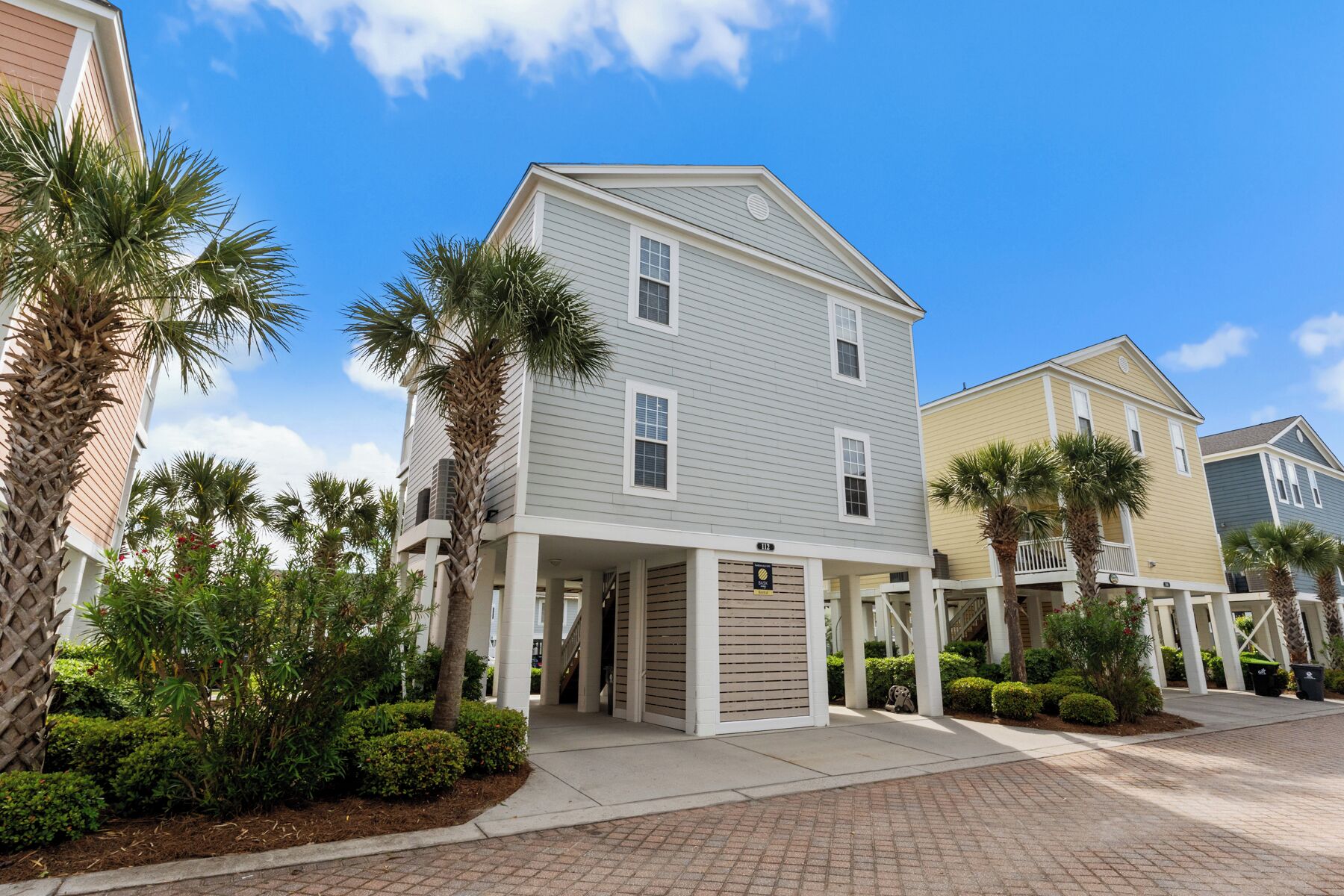 A residential building with a covered entrance, palm trees, and a clear blue sky.