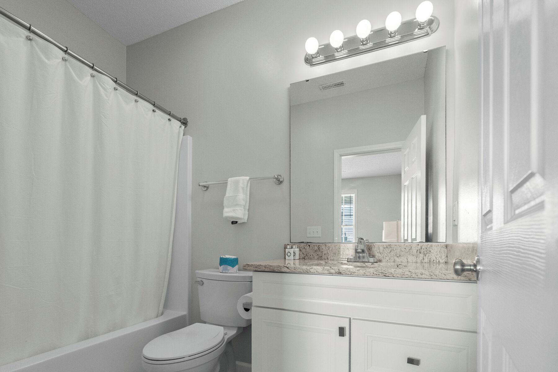 A bathroom with a shower curtain, a toilet, a sink with a mirror, and a vanity with cabinets.