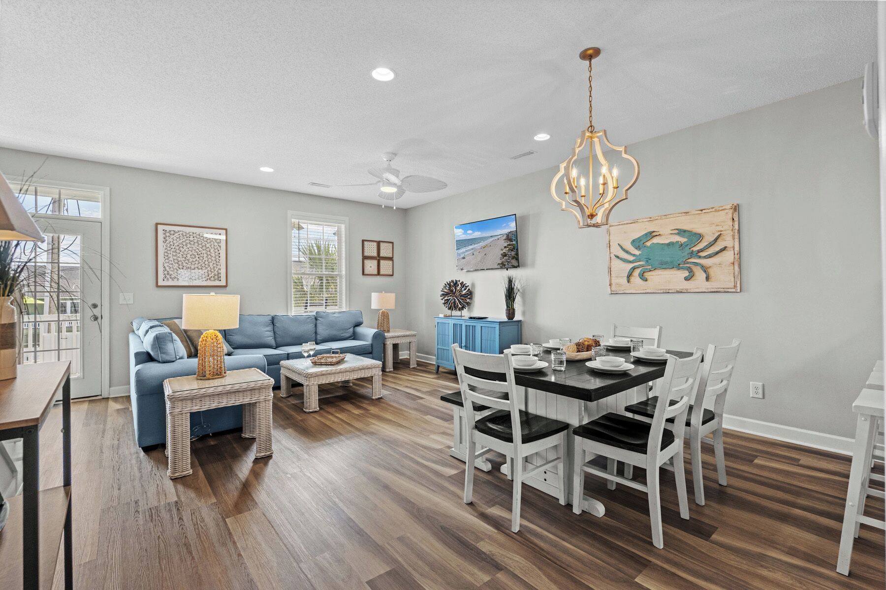 A spacious living room with a blue sofa, dining table with white chairs, and a ceiling fan.