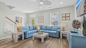 A living room with a blue sectional sofa, wicker coffee table, and a ceiling fan. - Crabby Paddy: Short Walk To Beach, Sunset Views (Garden City Beach)