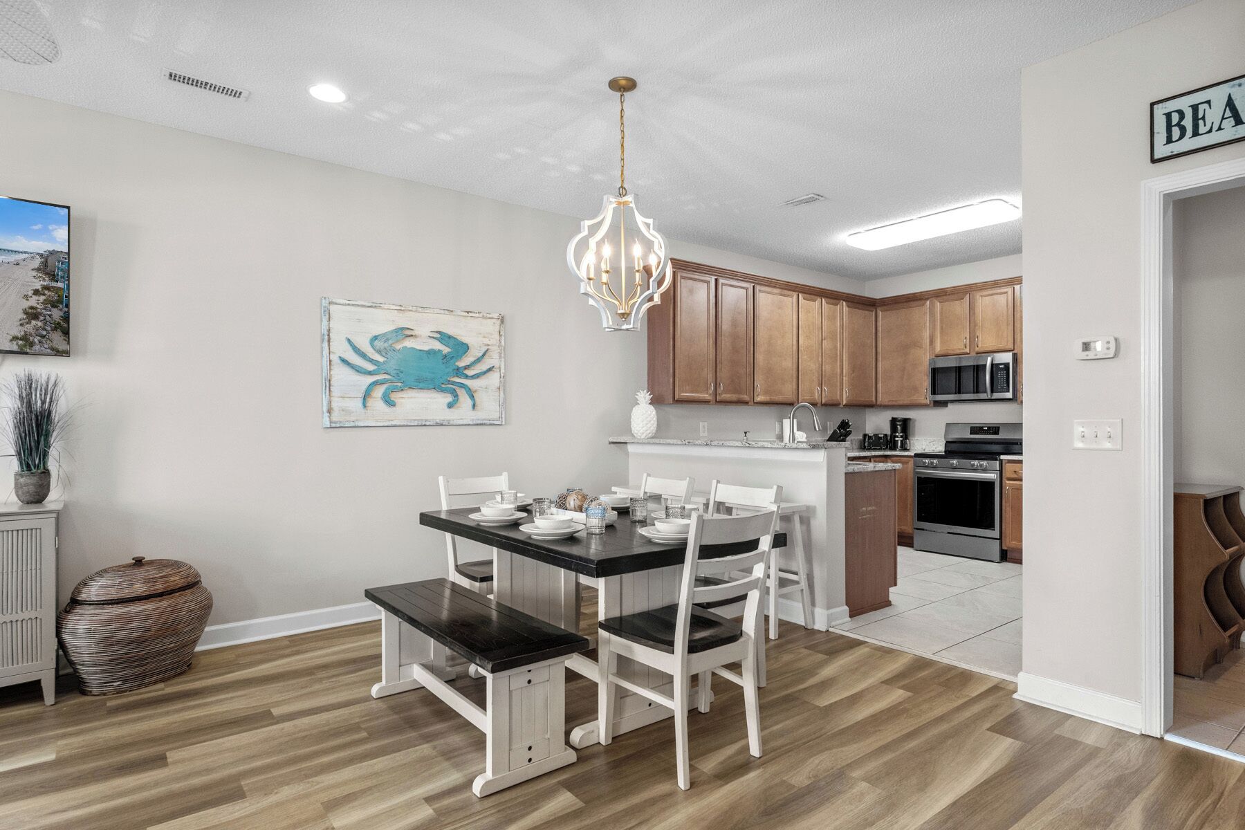 A modern kitchen with wooden cabinets, stainless steel appliances, and a dining area with a black table and white chairs.