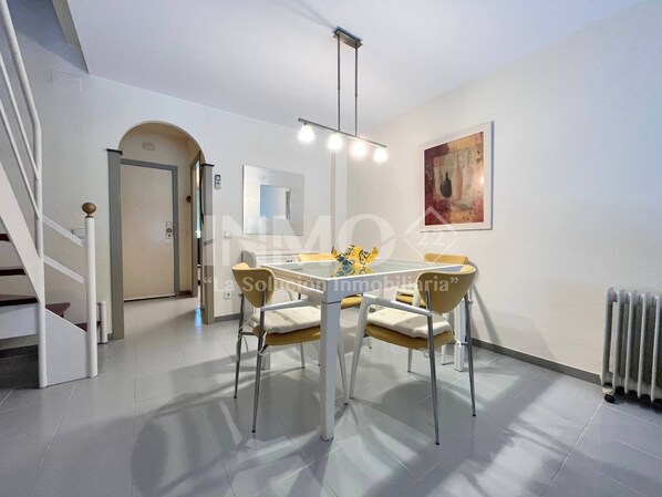 A modern dining area with a glass table, four chairs, and a pendant light.