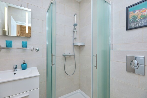 A modern bathroom with a glass shower enclosure, a white sink with blue soap dispensers, and a framed picture on the wall.