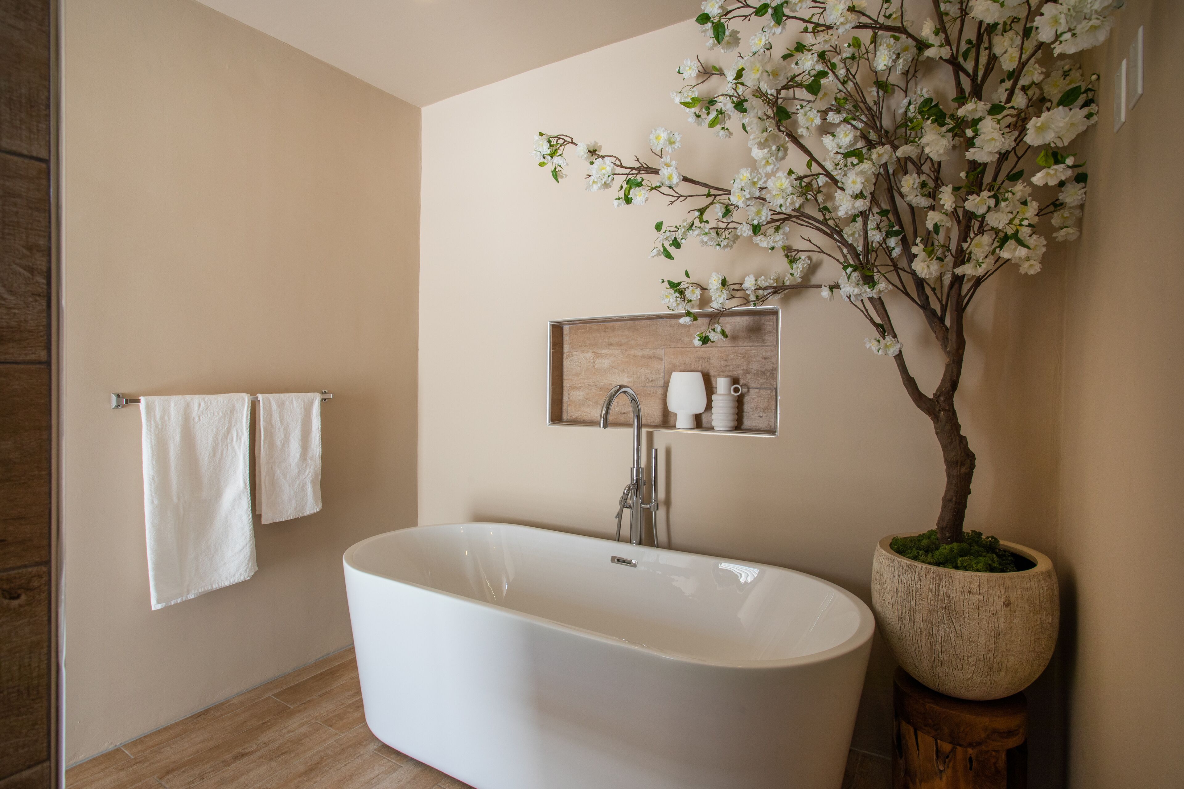 Ein modernes Badezimmer mit freistehender Badewanne, einem Holzregal mit Pflegeprodukten und einer Topfpflanze.