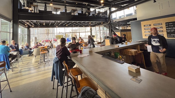 Zona de bar moderna con techos altos, amplias ventanas y diversas opciones de asientos.