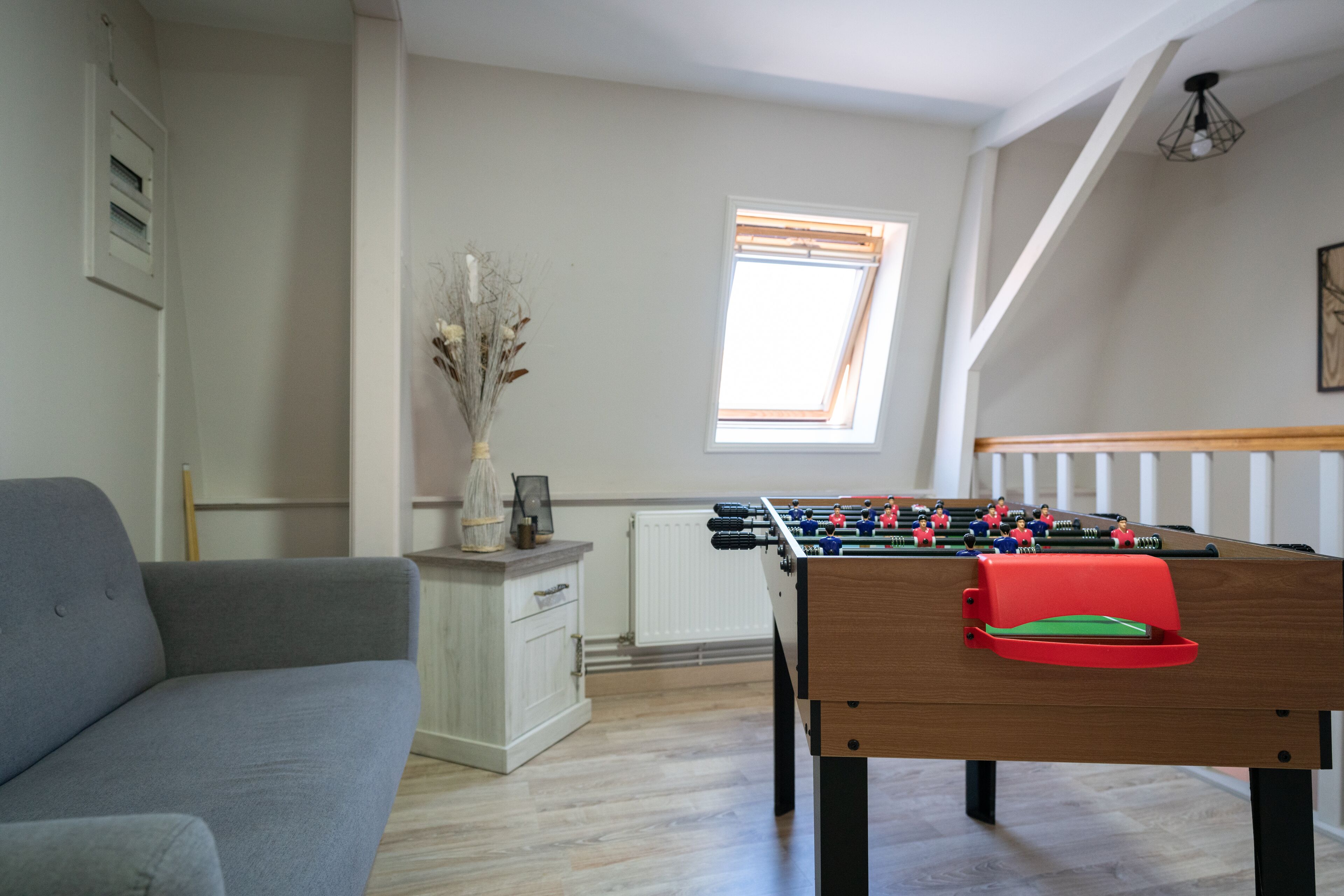 Ein Raum mit Kicker, grauem Sofa, weißem Schrank und einem Fenster mit Jalousien.