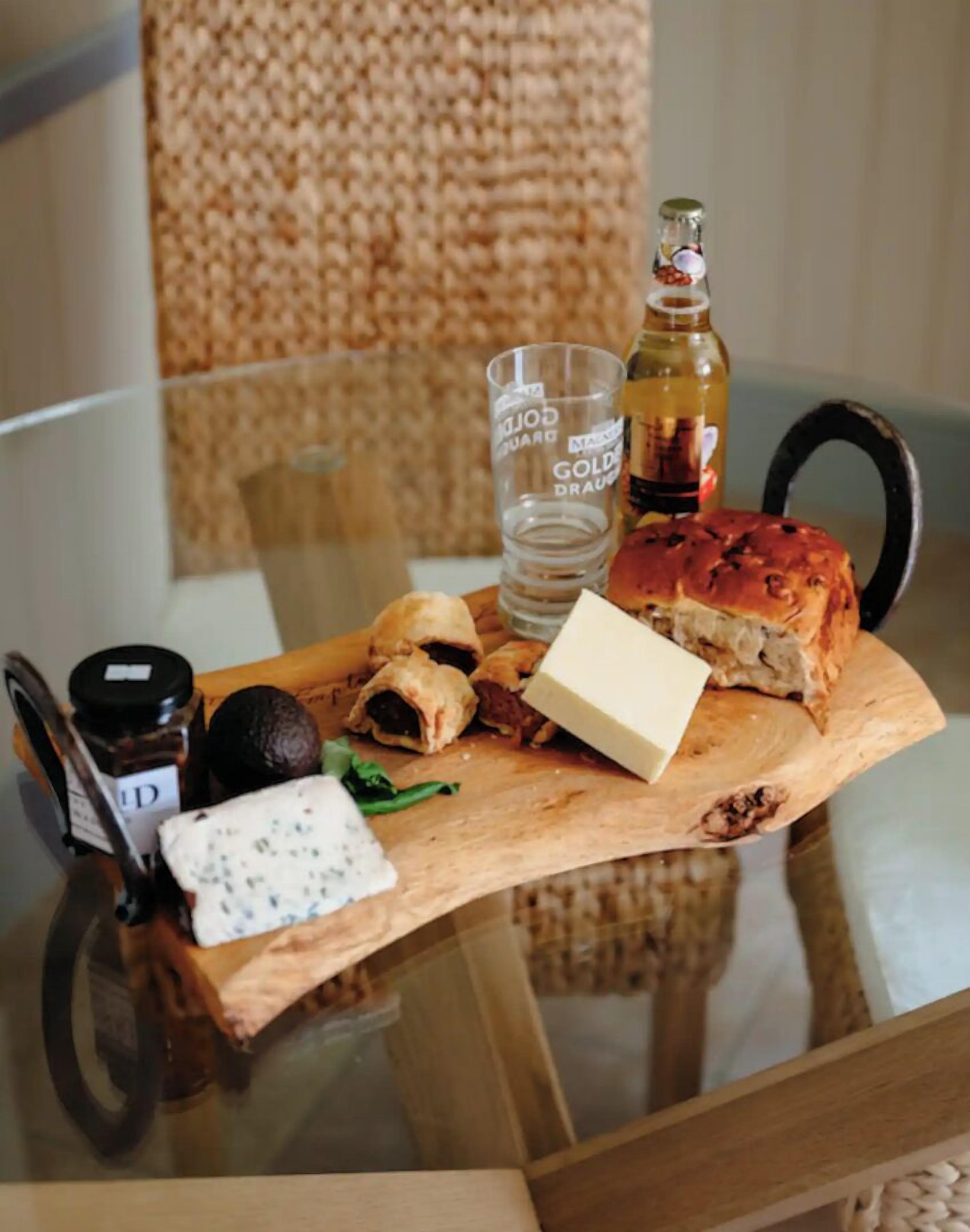 Ein Holzbord mit verschiedenen Speisen, einer Flasche und einem Glas auf einem Glastisch.