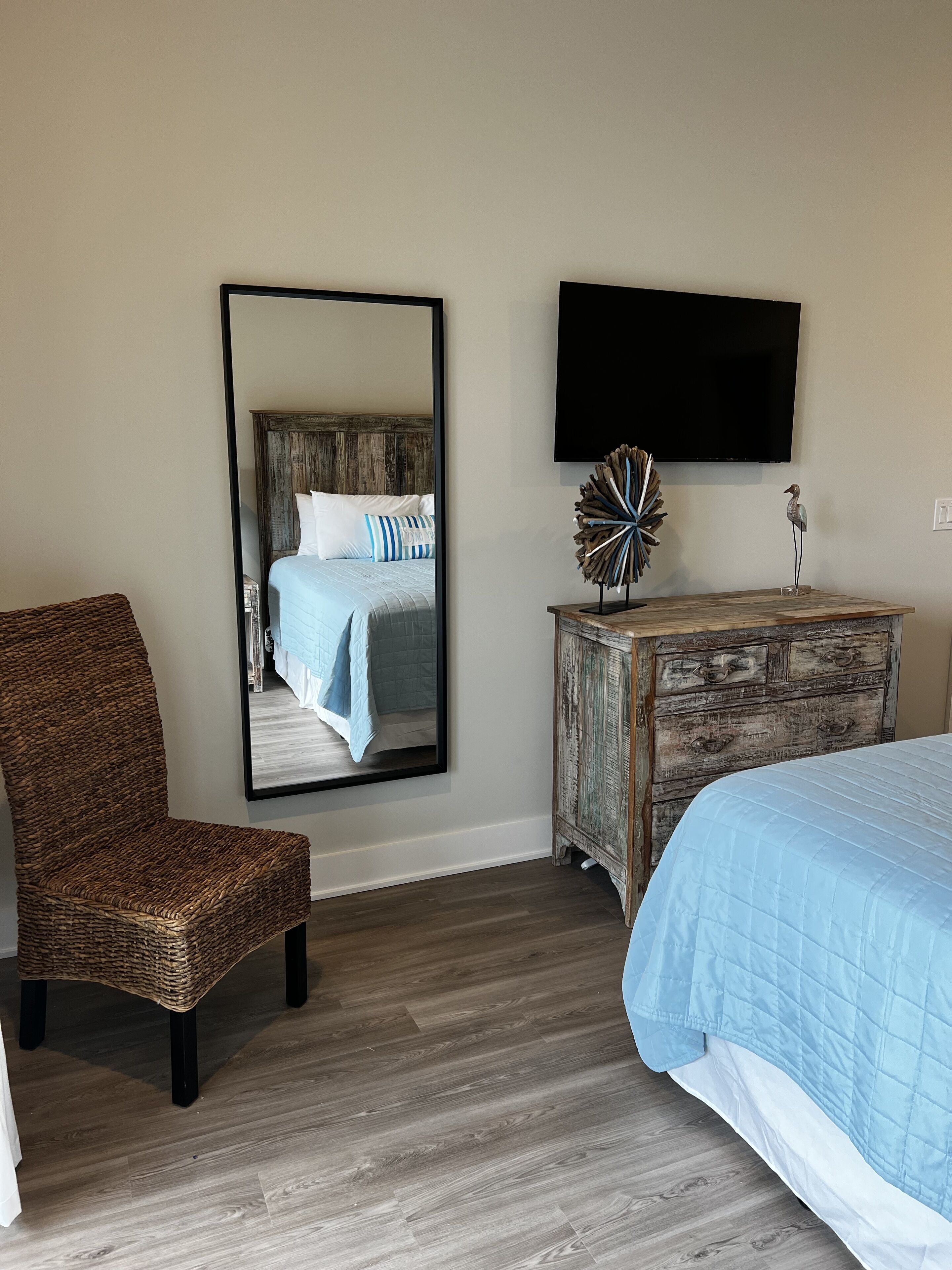 Un dormitorio con cama, una silla, un aparador y un televisor instalado en la pared.