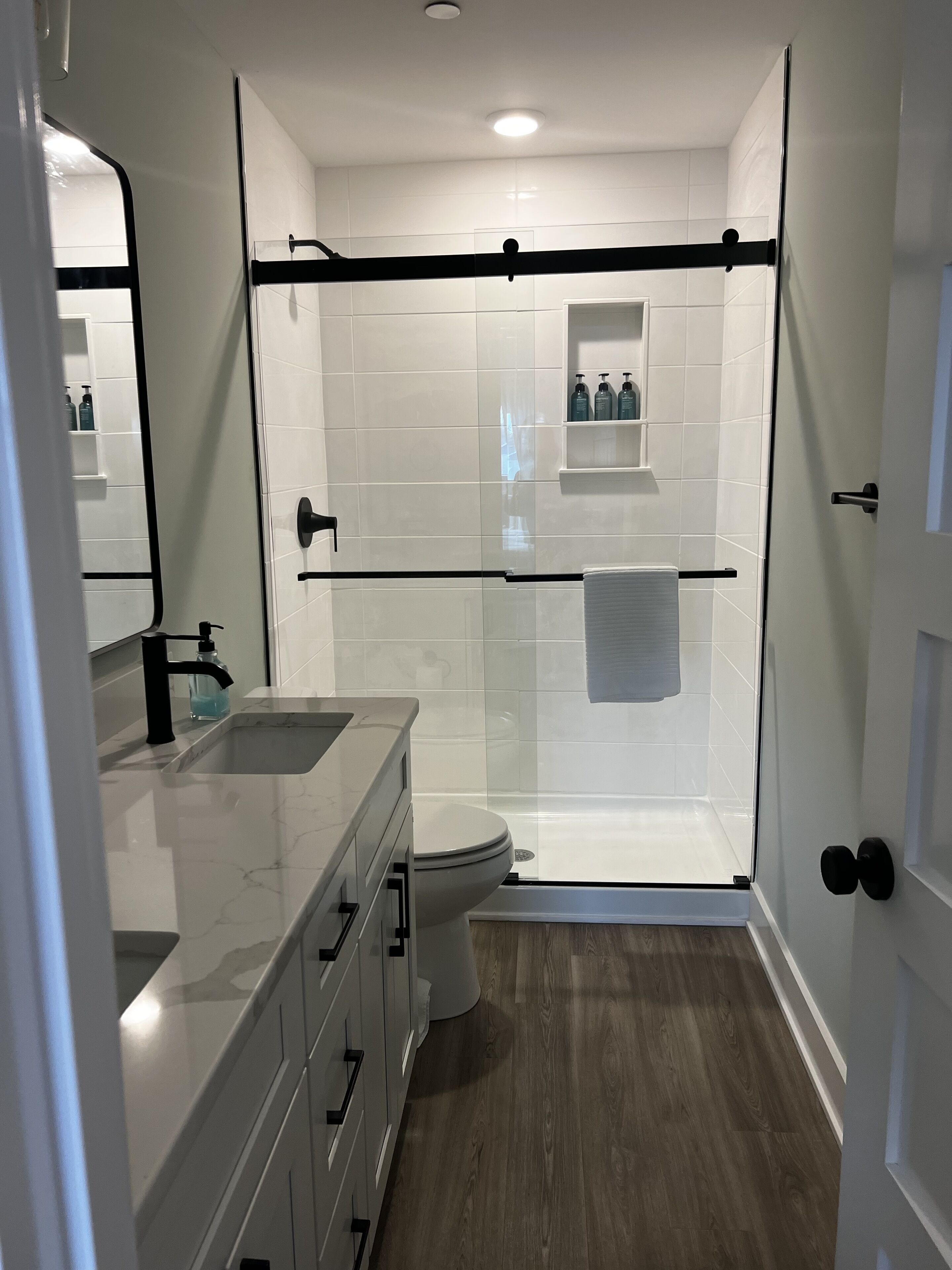 A modern bathroom with a glass-enclosed shower, a white toilet, and a vanity with a sink and mirror.