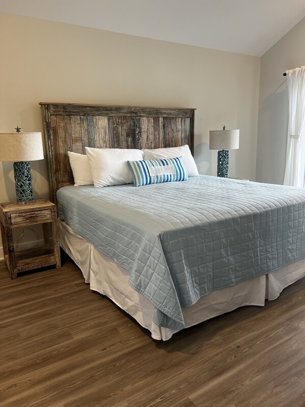 A bedroom with a wooden headboard, a blue quilted bedspread, white pillows, and two bedside tables with lamps.