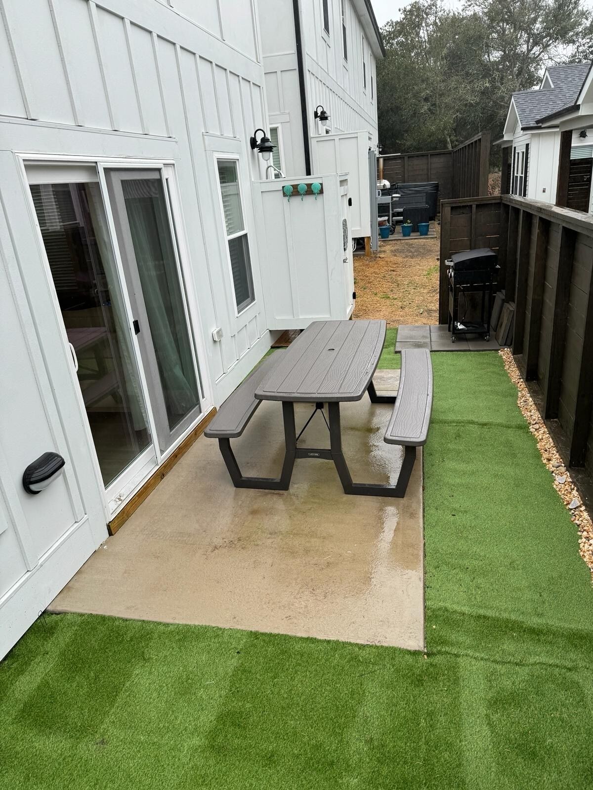 A patio with a picnic table and artificial grass, adjacent to a white building with a sliding glass door.