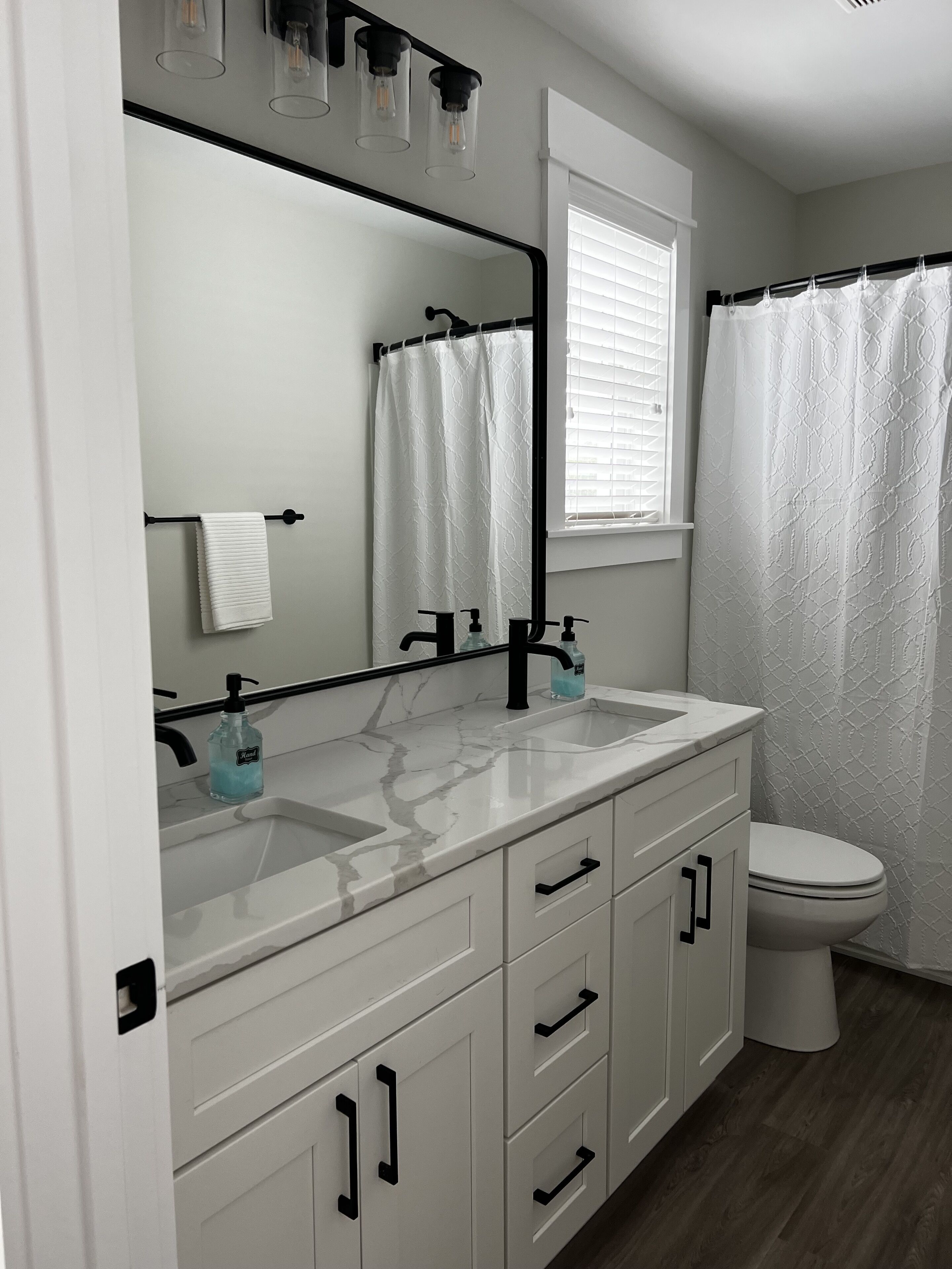 A bathroom with a white vanity, a black faucet, a mirror, a towel rack, a toilet, and a shower curtain.