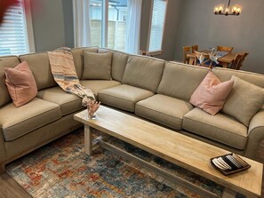 A living room with a beige sectional sofa, a wooden coffee table, and a colorful rug.
