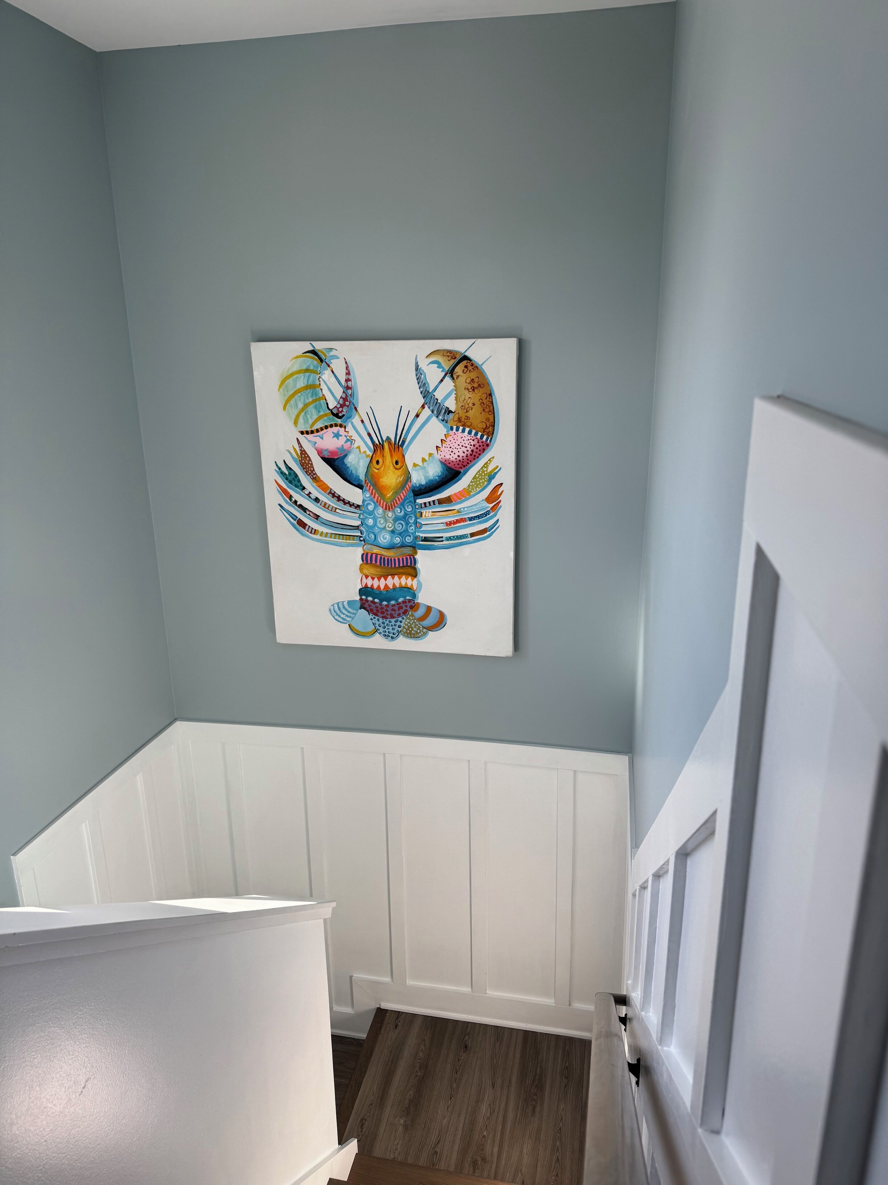 A room with a white crib, a wall-mounted colorful artwork, and a white wainscoting.