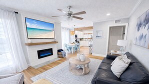 A modern living room with a fireplace, a large TV, a ceiling fan, and a view of the beach through the window. - ⛵️Coastal Retreat at Tech Terrace 3/2 Remodeled 2 Kings (Lubbock)