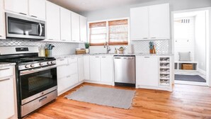 A modern kitchen with white cabinets, stainless steel appliances, and a wooden floor. - ⛵️Coastal Retreat at Tech Terrace 3/2 Remodeled 2 Kings (Lubbock)