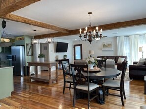A spacious living area with a wooden dining table, dark chairs, and a chandelier. A flat-screen TV is mounted on the wall, and a sofa is visible in the background. - ❤️Heart of Med District Lit’l Sister 3/2 Remodeled (Lubbock)