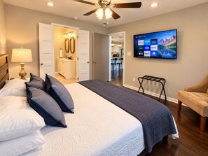 A bedroom with a bed, a ceiling fan, a TV mounted on the wall, and a door leading to a bathroom.