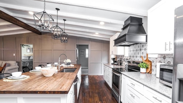 Eine moderne Küche mit einer Holztischinsel, Edelstahlgeräten und einer Decke im Bauernhausstil.