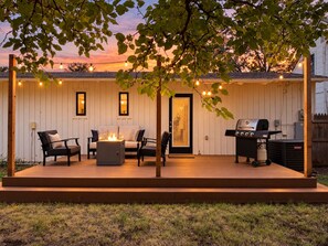 A covered outdoor patio with a grill, seating area, and a fire feature. - Heart of Medical District 4BR Home | Walk to Tech & Med Ctr (Lubbock)