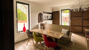 A modern dining area with a wooden table and colorful chairs, large windows, and a chandelier. - Hotel Kronenkurve (Bergkamen)