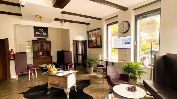 A spacious lobby with wooden floors, a reception desk, leather seating, and a large window with a view. - Hotel Kronenkurve (Bergkamen)