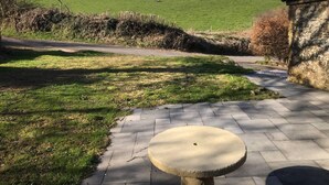 A paved pathway leading to a stone building with a grassy field and trees in the background.