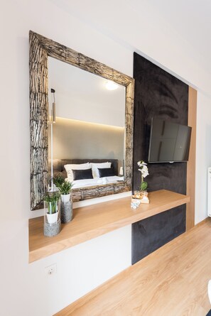 A modern bedroom with a large mirror, a flat-screen TV, and a wooden bedside table with decorative items.