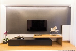 A modern living room with a flat-screen TV mounted on a grey wall, a wooden coffee table with decorative items, and a small potted plant.
