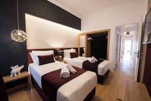 Ein Hotelzimmer mit zwei Betten, einem großen Spiegel, Holzboden und einem Flur zu weiteren Zimmern.