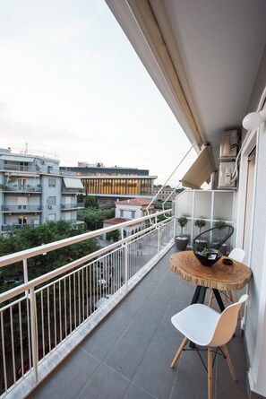 A balcony with a round table and two chairs, potted plants, and a view of surrounding buildings. - Acropolis Panoramic View Exclusive Apartment | 3 Falirou str 11742 Athens (Athens)