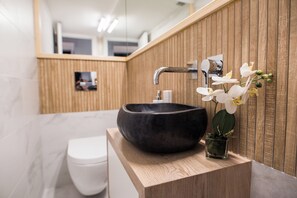 Ein modernes Badezimmer mit einem Holzwaschtisch, einem schwarzen Haussinkenschrank, einer weißen Toilette und einer kleinen Topforchidee.