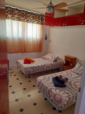 A bedroom with two beds, a ceiling fan, a window with curtains, and a tiled floor. - Los Cristianos Penthouse.Sea/Mountain Views.Heated Pool. Wi Fi (Los Cristianos)