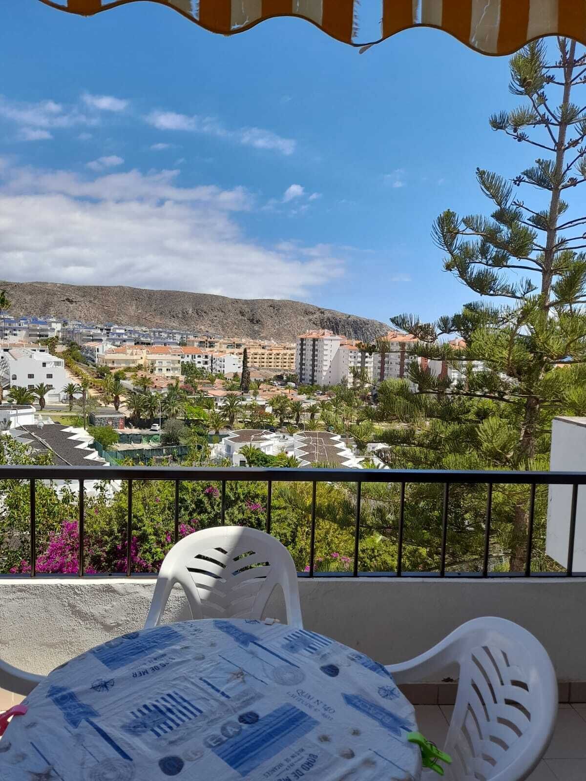 Un balcón con vista a un pueblo, que muestra edificios, una montaña y algo de vegetación.