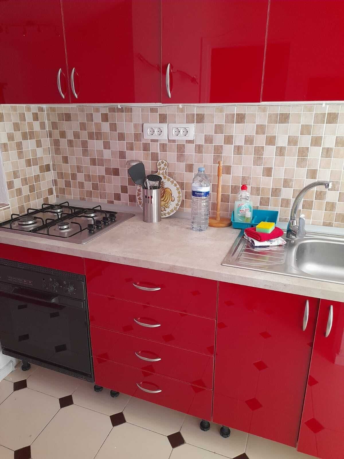 Une cuisine avec des meubles de couleur rouge, une cuisinière à gaz, un lave-vaisselle et un dosseret carrelé.