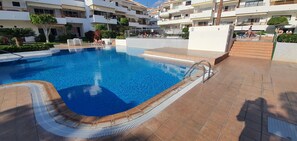 A swimming pool with a tiled deck, surrounded by a multi-story building with balconies and outdoor seating. - Los Cristianos Penthouse.Sea/Mountain Views.Heated Pool. Wi Fi (Los Cristianos)
