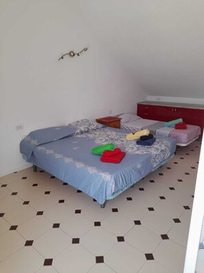 Quarto com duas camas, penteadeira vermelha e luminária fixada na parede.