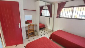 Une chambre avec deux lits simples, un bureau avec une chaise, un miroir et une fenêtre avec des rideaux.