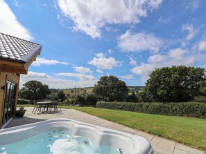 A hot tub in a backyard with a view of a house, a lawn, and trees. - Pen Bryn (Ruthin)