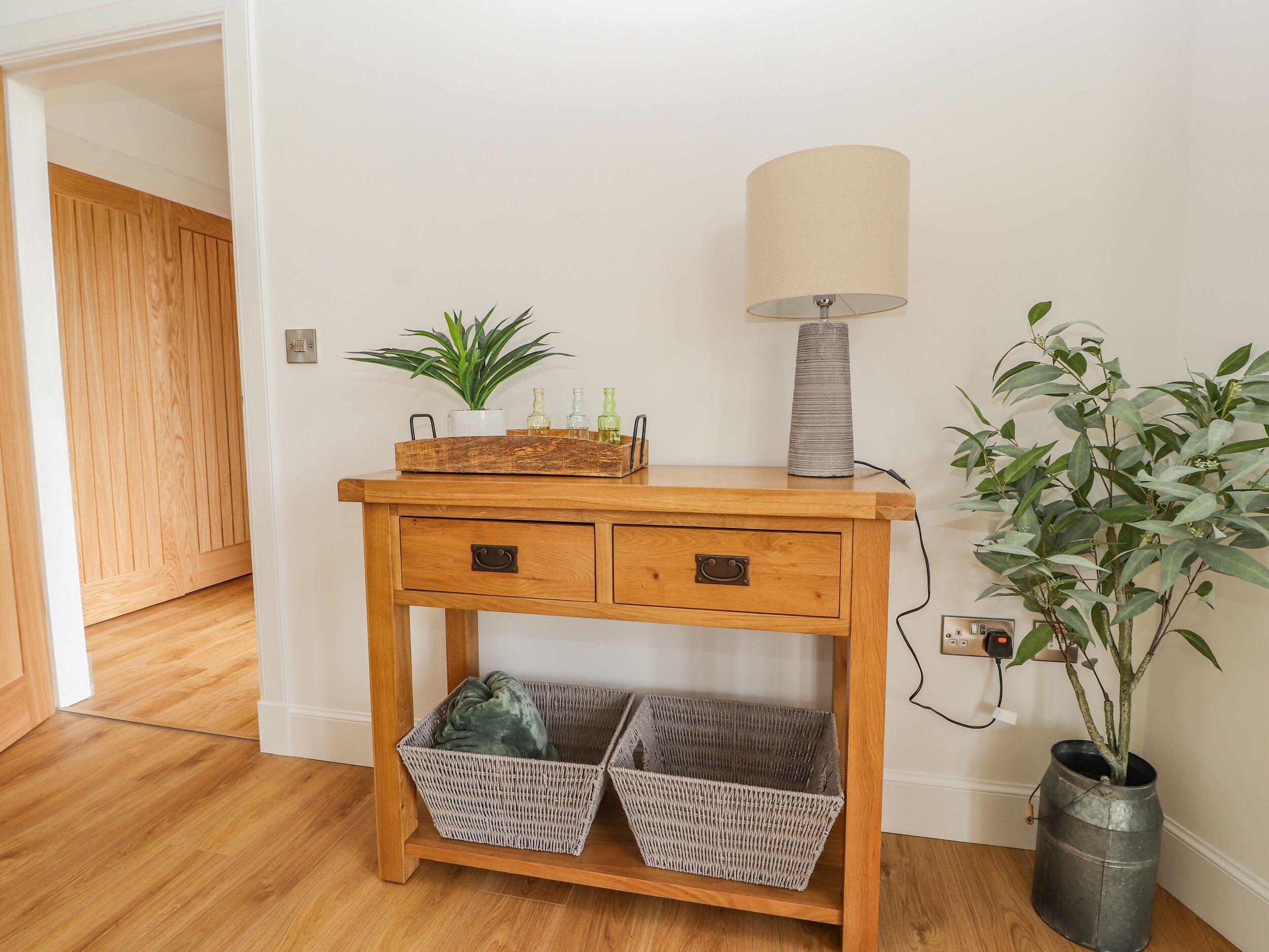 A wooden console table with two drawers, a lamp, and wicker baskets.
