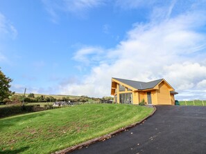 A modern house with a sloped roof and large windows, surrounded by a well-maintained lawn and a paved driveway. - Pen Bryn (Ruthin)